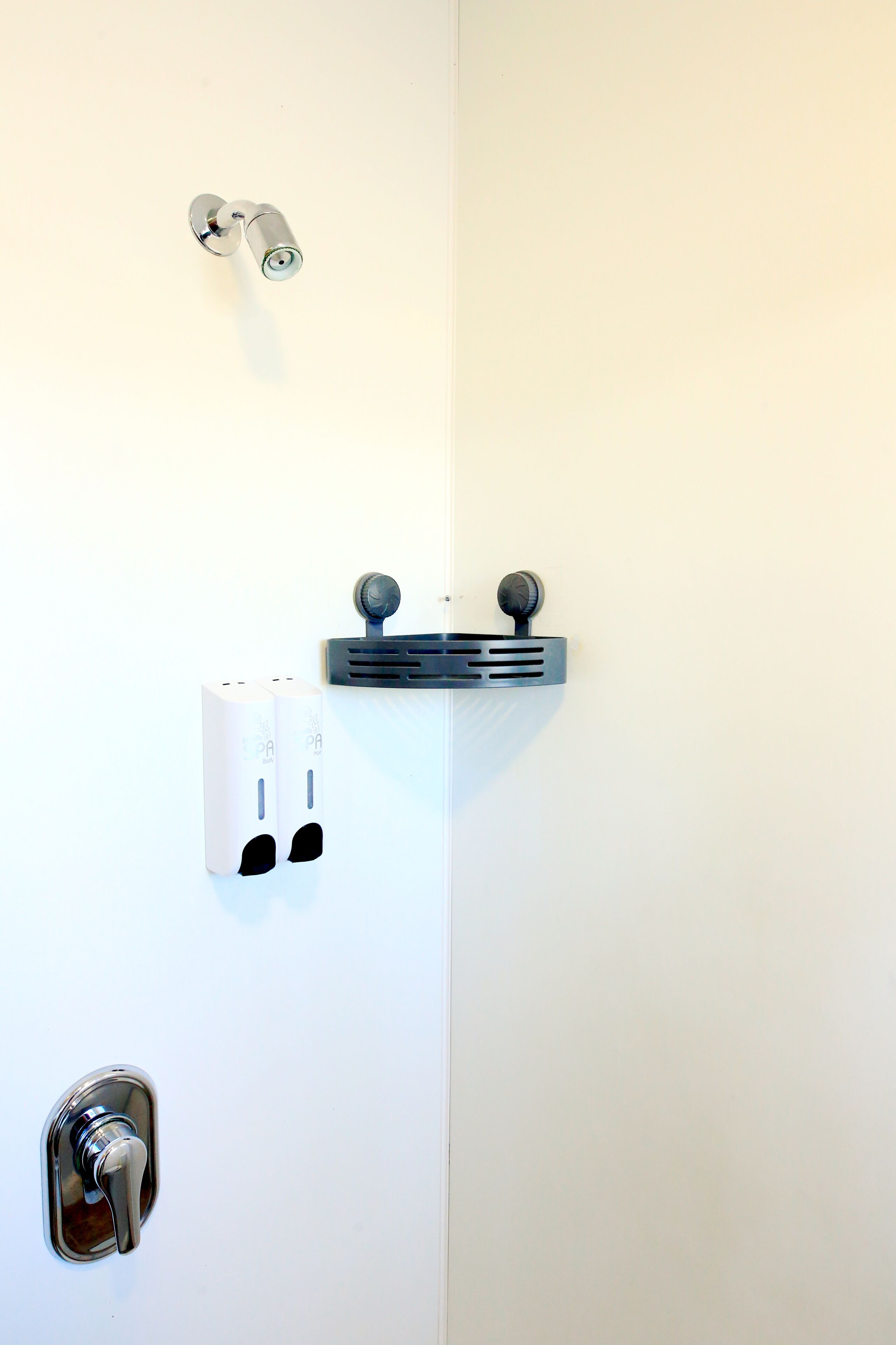 Une salle de bain équipée d’une douche, d’un robinet, d’un distributeur de savon et d’un porte-serviettes.