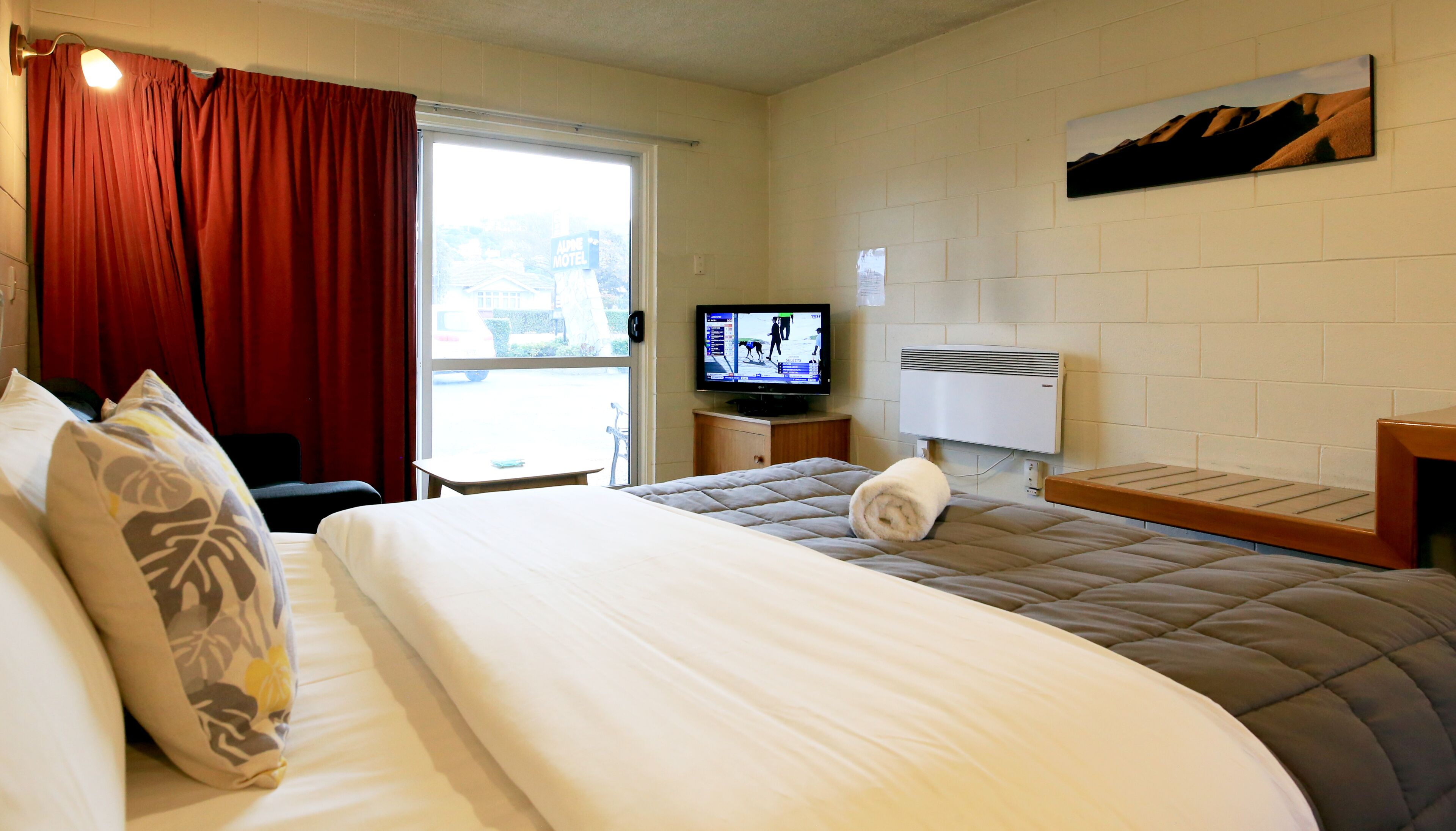 Una habitación de hotel con dos camas, televisión, ventana y un cuadro en la pared.
