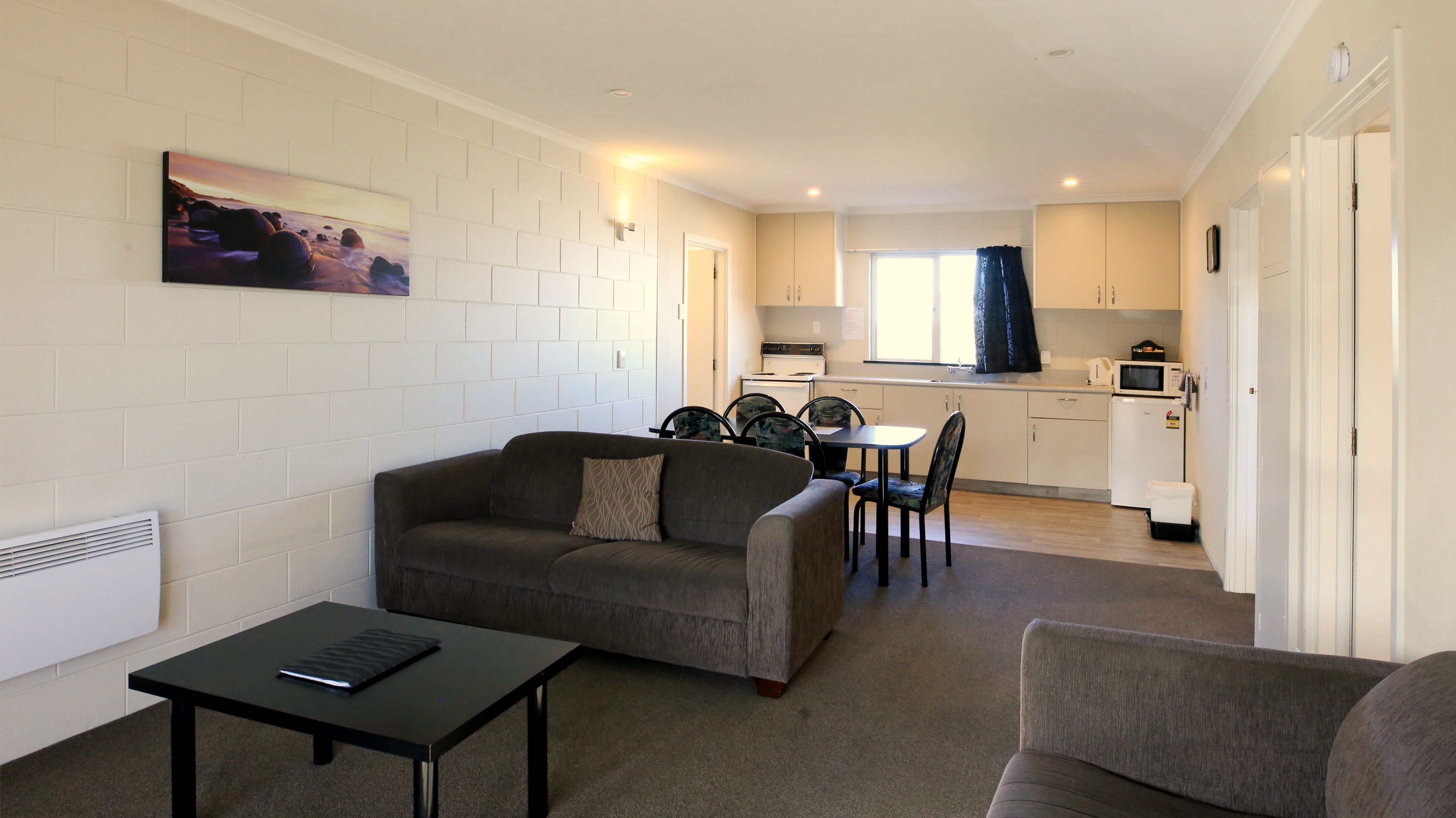 A compact living space with a sofa, dining table, chairs, kitchenette, and a painting on the wall.