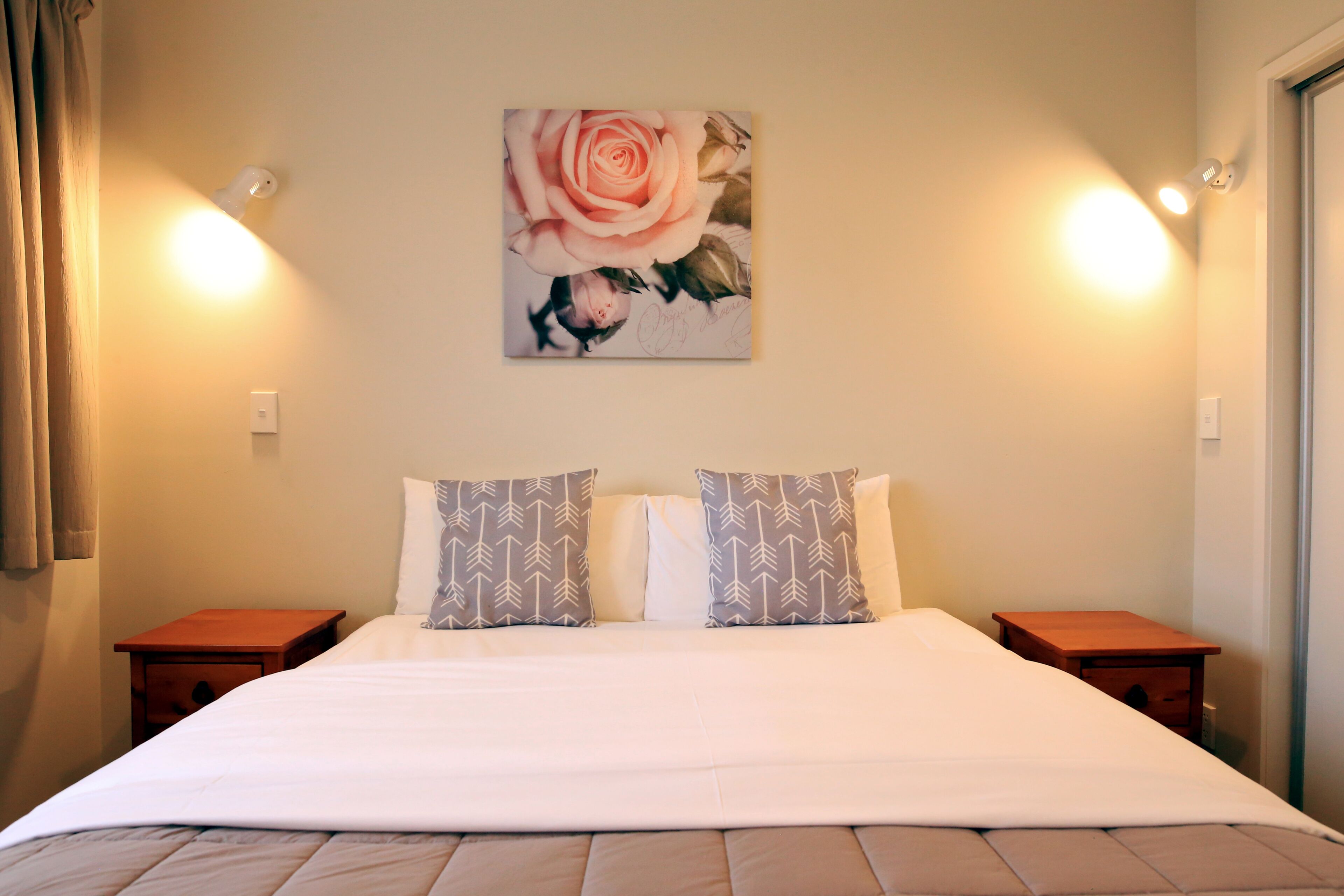 Ein Hotelzimmer mit einem großen Bett, zwei Nachttischen, einem Rosenbild an der Wand und zwei Wandleuchten.