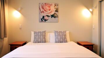 Ein Hotelzimmer mit einem großen Bett, zwei Nachttischen, einem Rosenbild an der Wand und zwei Wandleuchten.