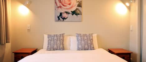 Habitación de hotel con una cama grande, dos mesitas de noche, un cuadro de una rosa en la pared y dos luces empotradas.