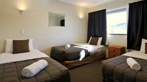 A hotel room with three beds, a window with curtains, a mirror, and a small wooden nightstand.