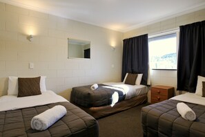 A hotel room with three beds, a window with curtains, a mirror, and a small wooden nightstand.