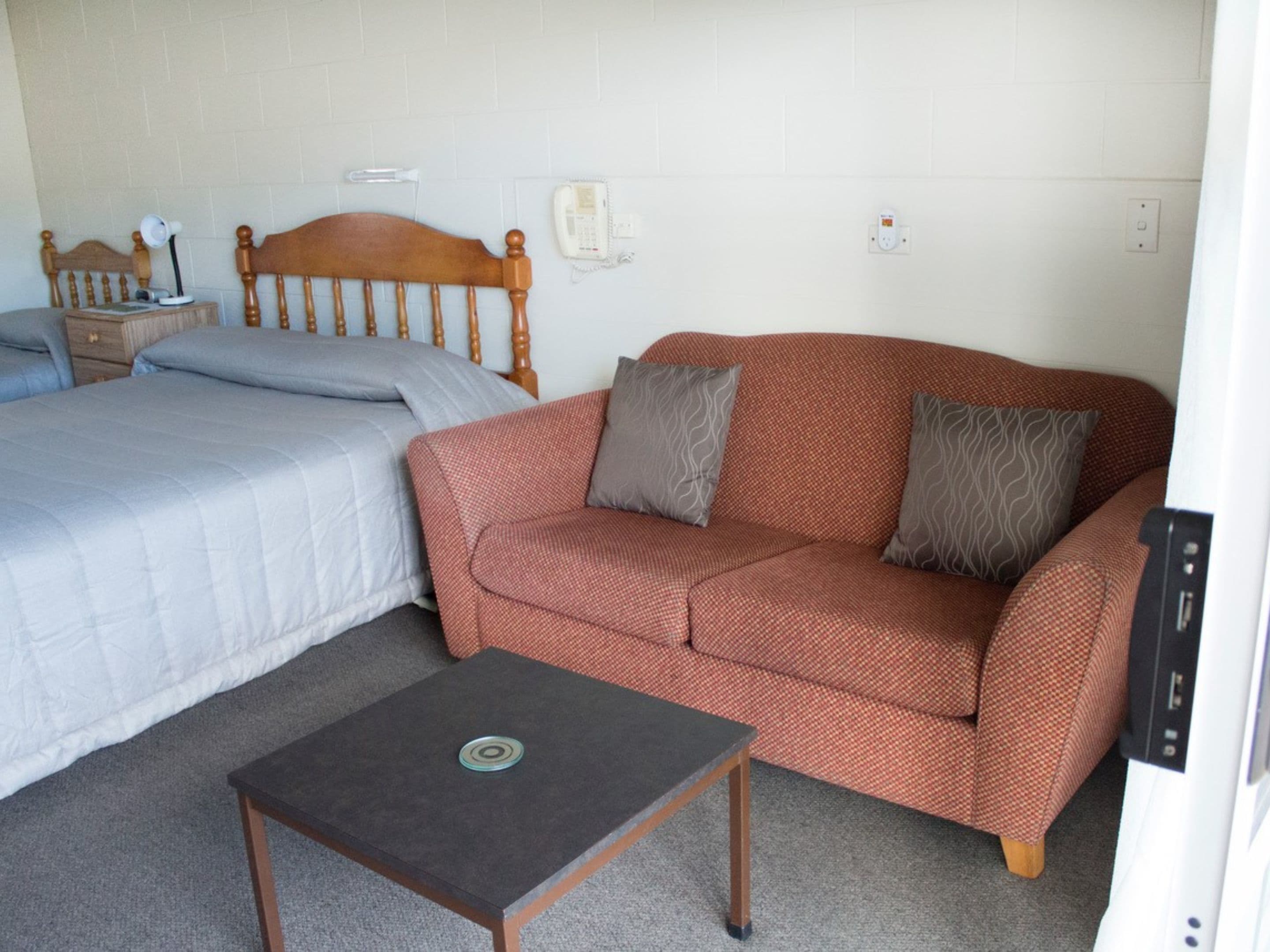 Una habitación con cama, un sofá rojo estampado, una mesita y un teléfono en la pared.