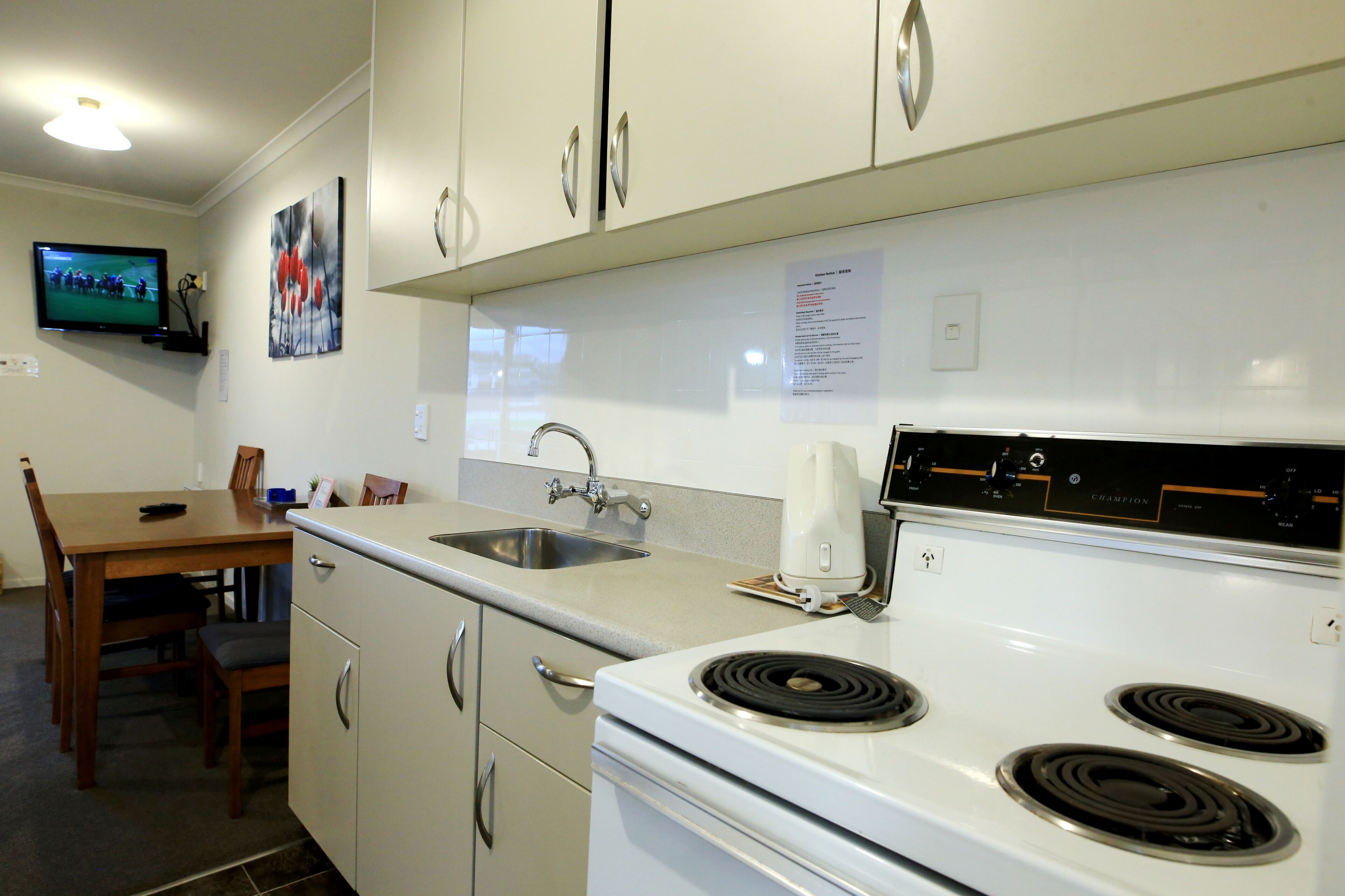 Una cucina funzionale con fornelli, lavello e una TV a schermo piatto montata a parete.