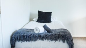 A neatly made bed with a white comforter, a rolled white blanket, and a dark blue throw blanket.