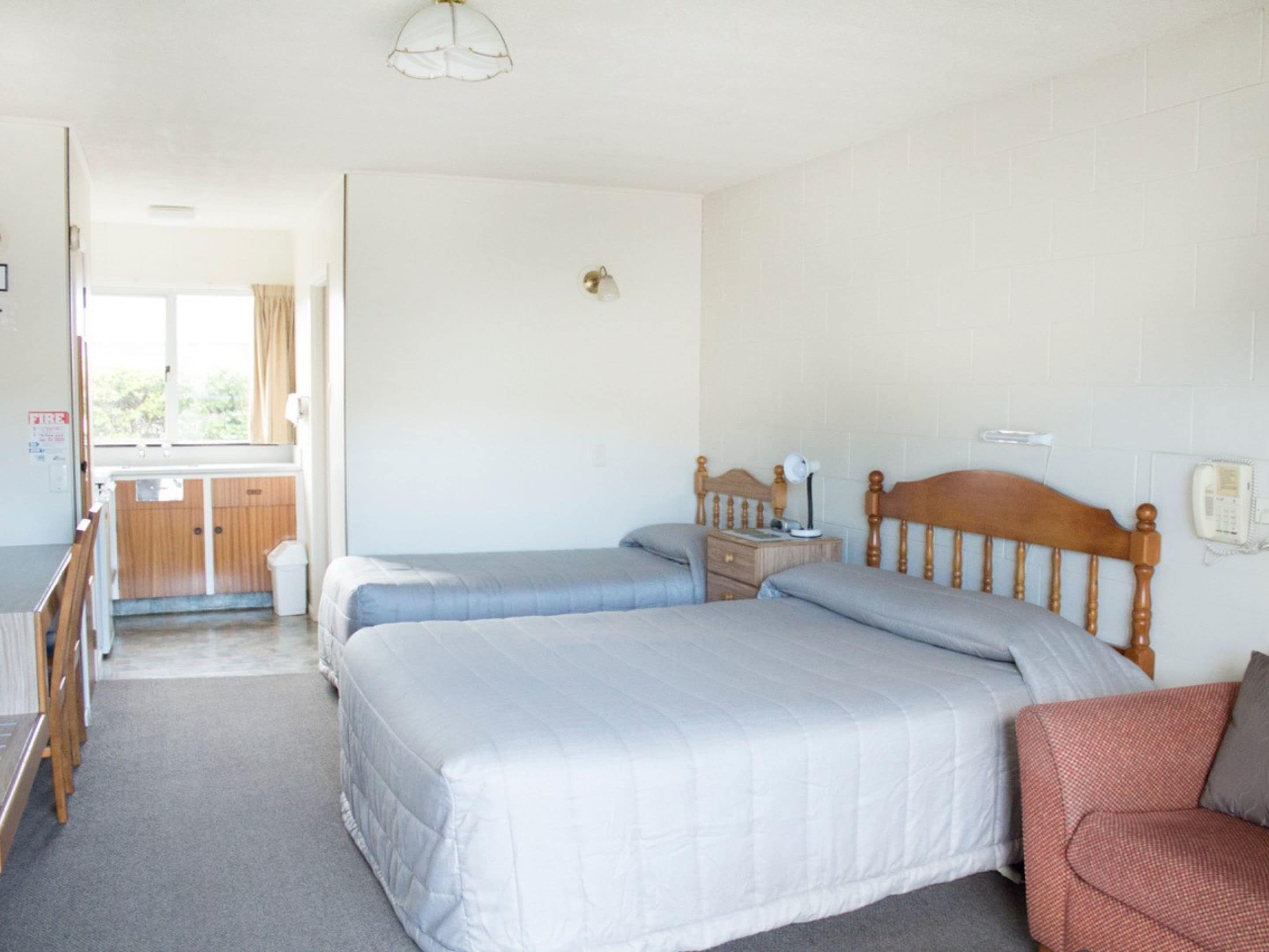 A bedroom with two beds, a wooden headboard, a bedside table, a lamp, and a chair.