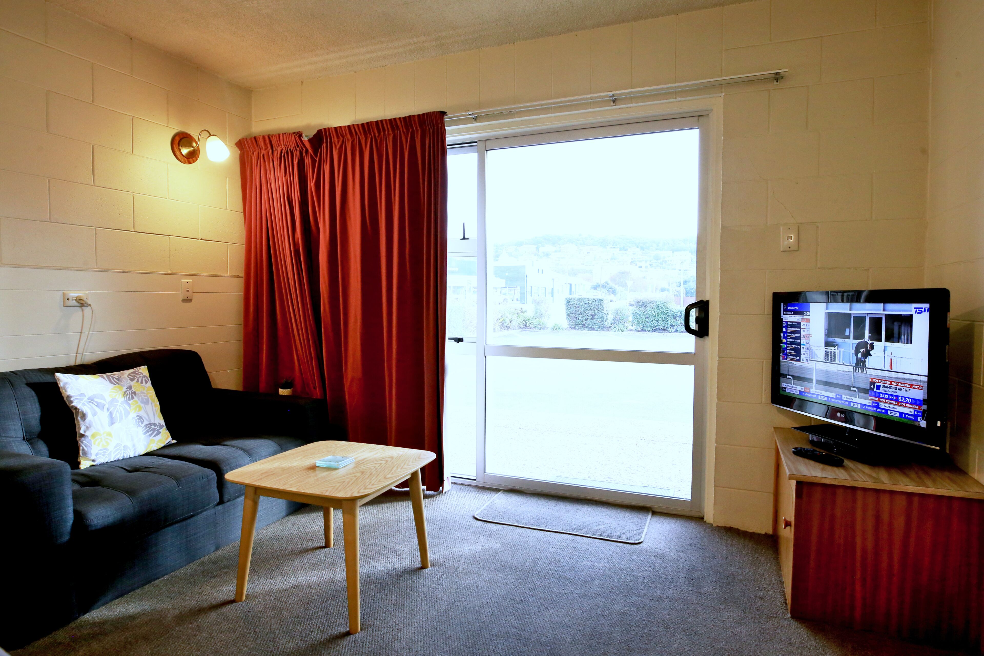 Una sala de estar con un sofá, una mesita, un televisor y una puerta corrediza de vidrio.