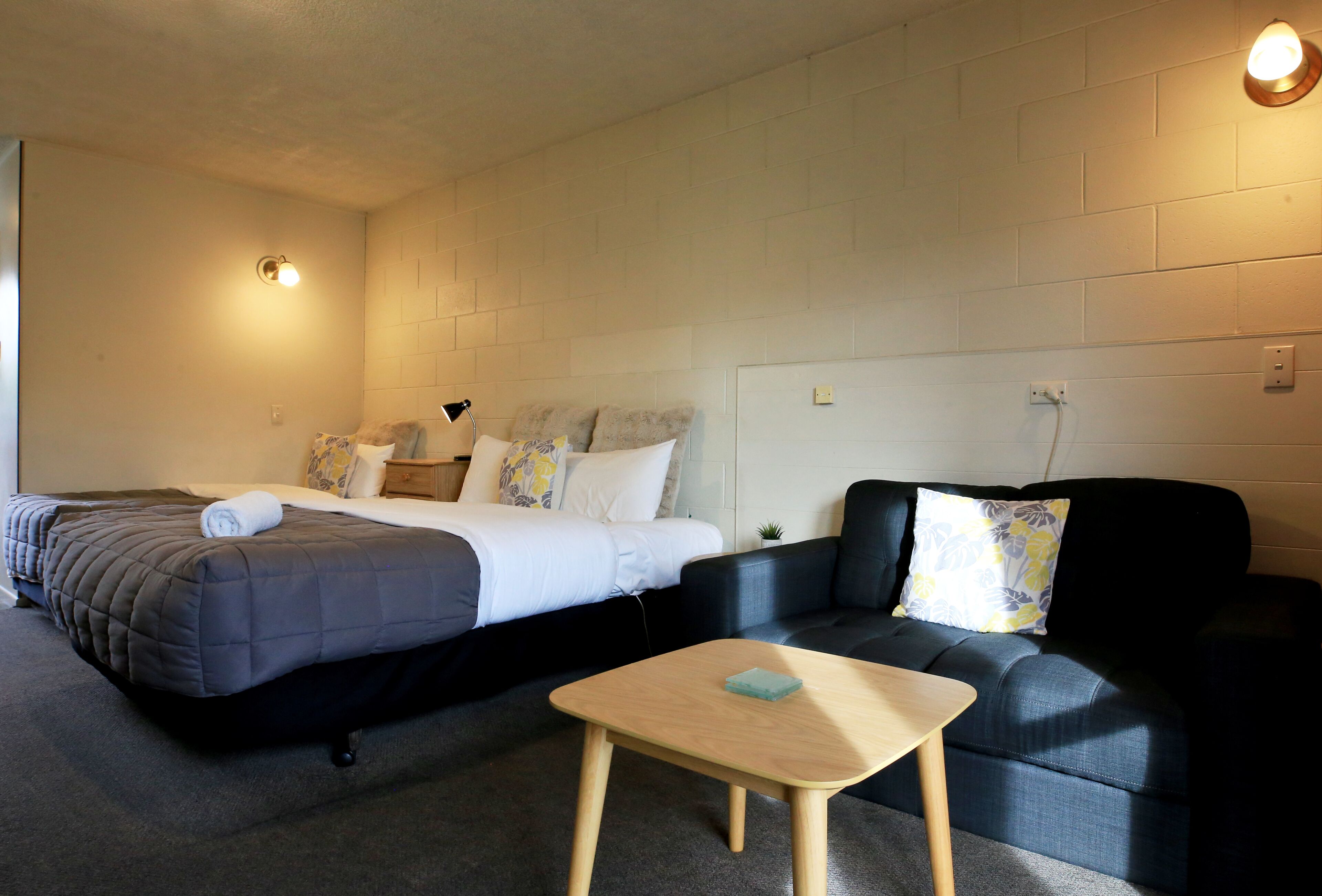 A hotel room with two beds, a sofa, a small table, and a wall-mounted light fixture.
