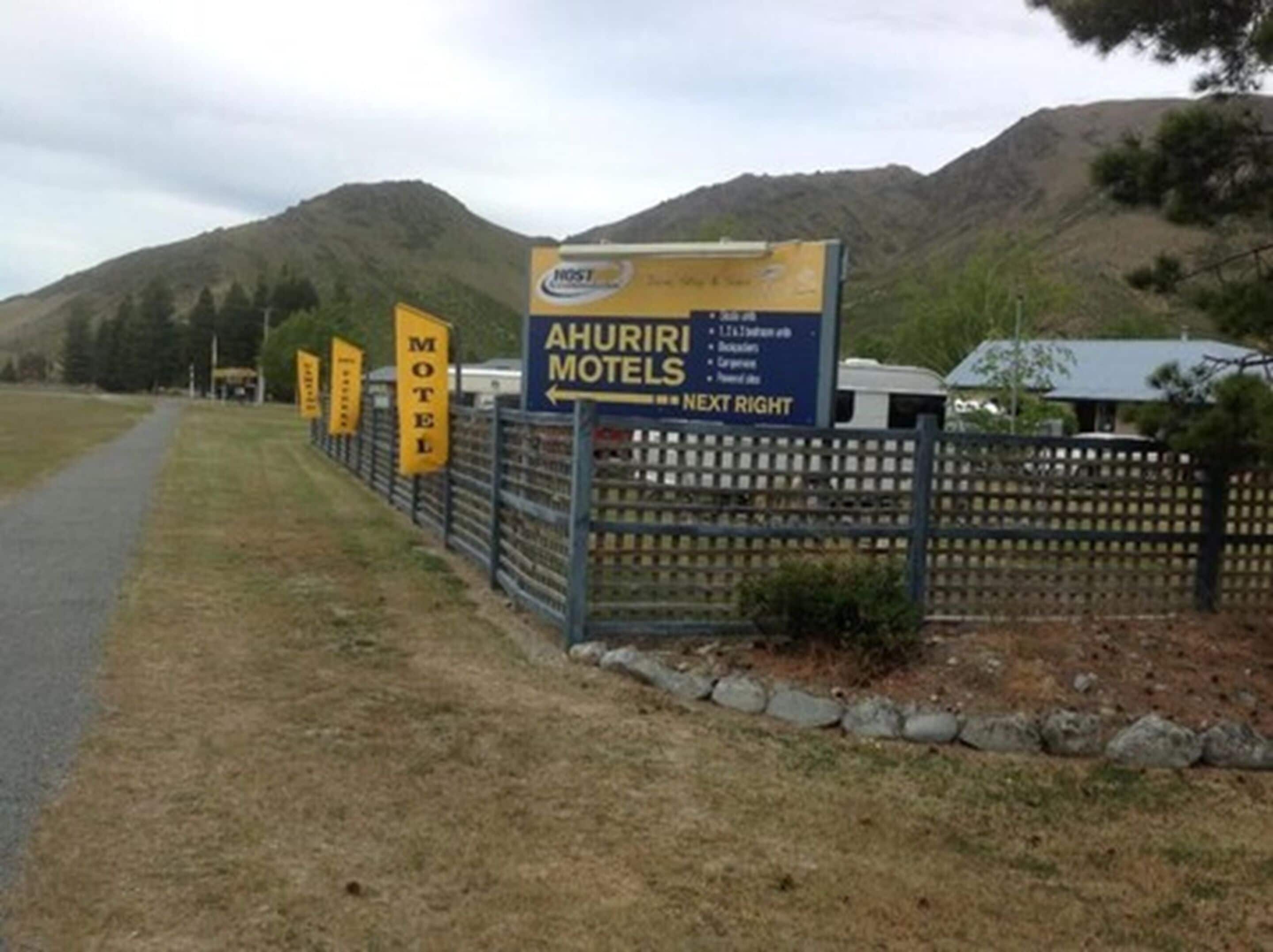 Schild eines Motels vor einer Bergkulisse, das den Namen 'AHURI MOTELS' anzeigt und nach 'RECHTS AABBIE' weist.