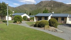 A building with a gravel driveway, surrounded by well-maintained grass and bushes. - Ahuriri Motels (Omarama)