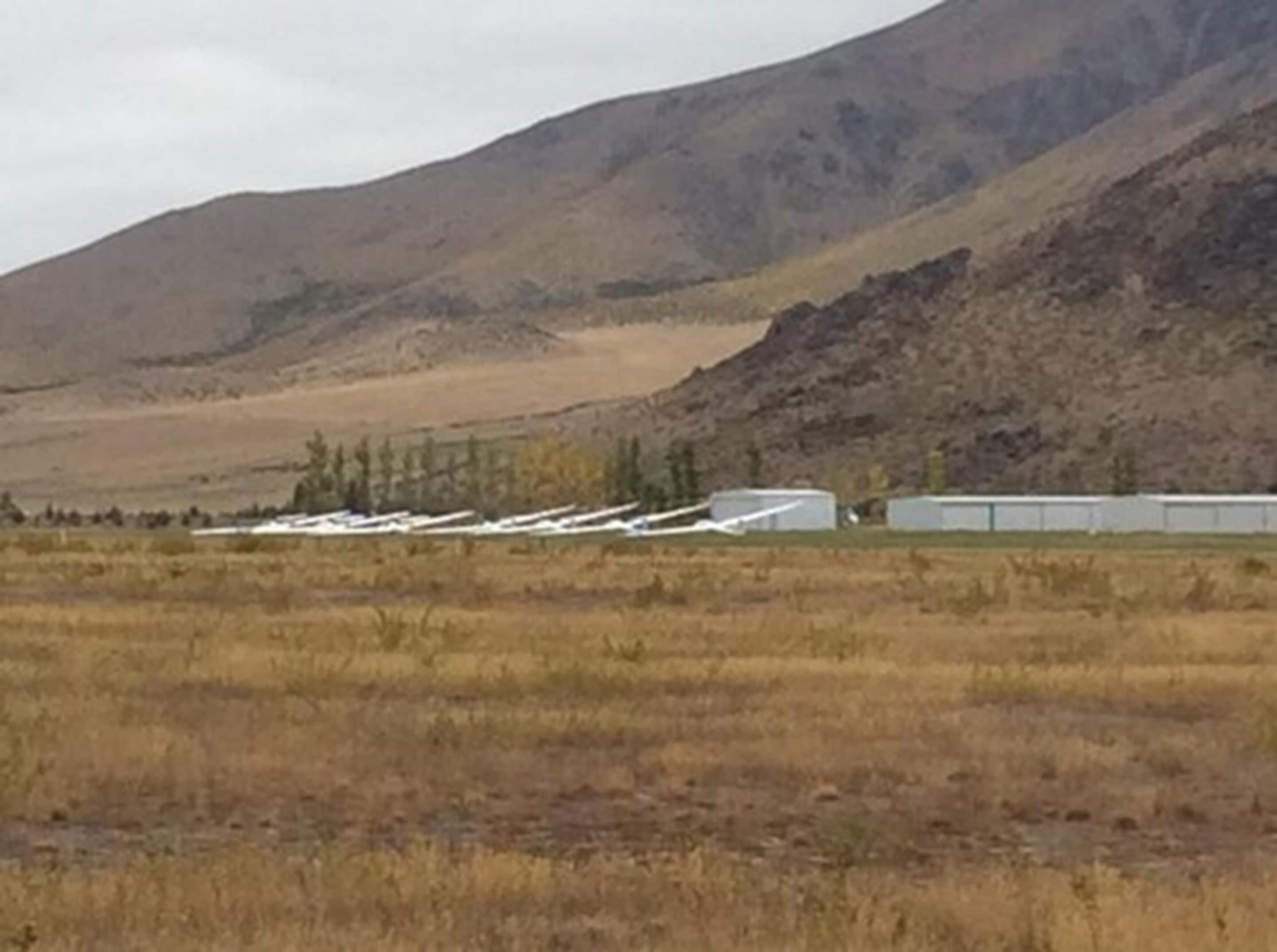 Paisaje rural con una montaña al fondo y una hilera de edificios blancos en primer plano.