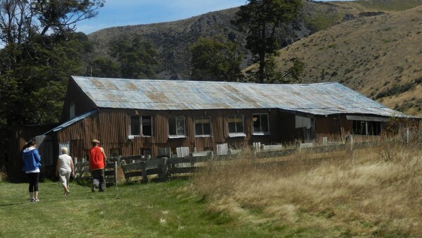 A rustic barn with a corrugated metal roof, surrounded by a wooden fence and grassy area.