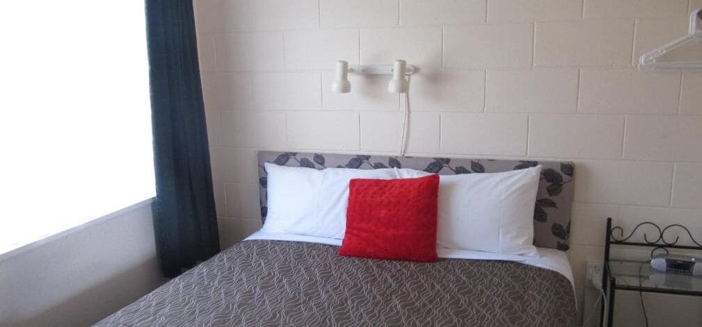 A hotel room with a bed, a nightstand, and a window with curtains.