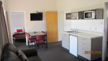 A compact hotel room with a kitchenette, a dining area, and a bed.