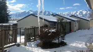 A house with a snow-covered roof and mountains in the background. - Ahuriri Motels (Omarama)