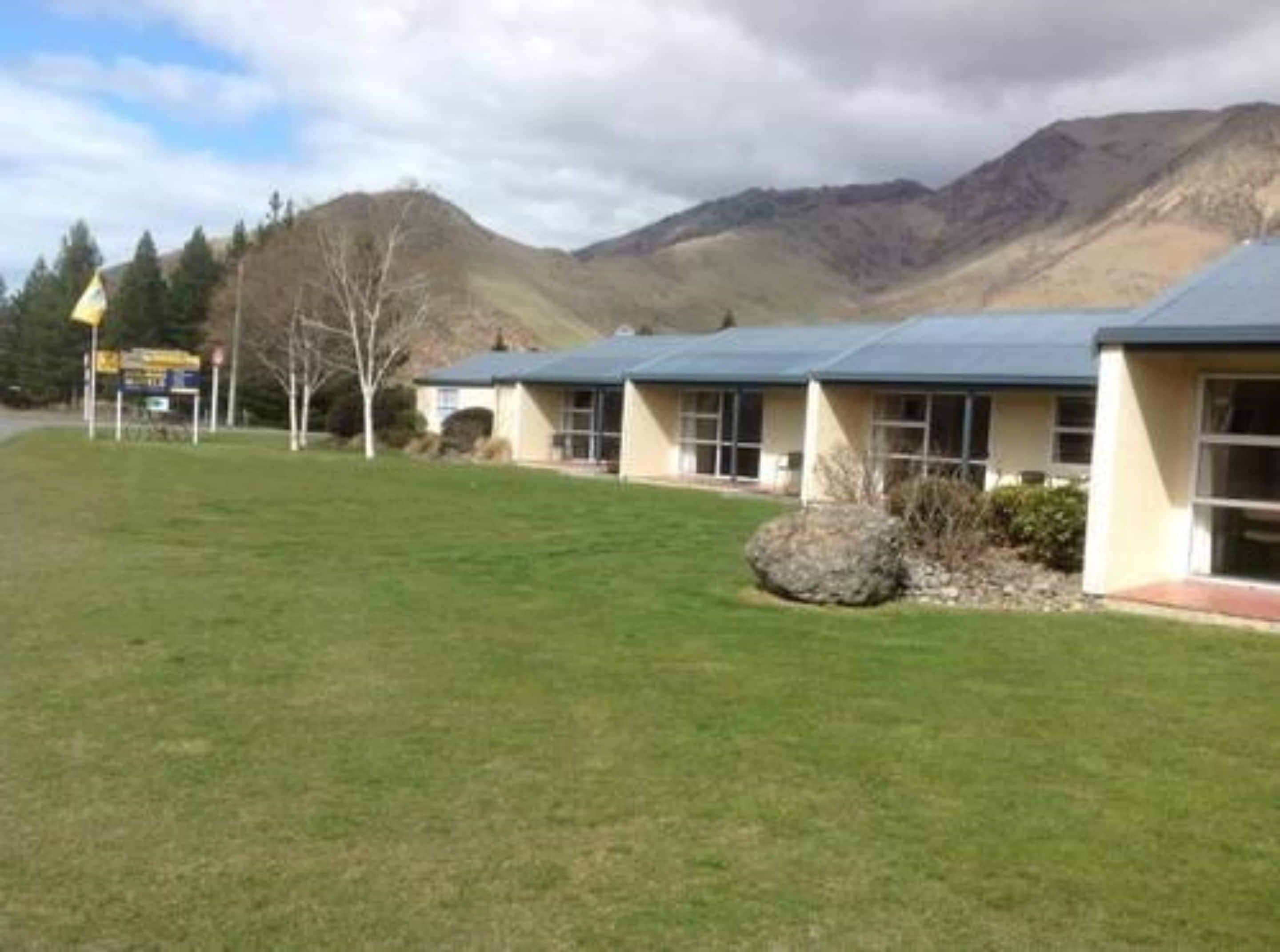 A row of single-story buildings with a flat roof, surrounded by a well-maintained lawn and a mountain in the background.