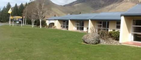 A row of single-story buildings with a flat roof, surrounded by a well-maintained lawn and a mountain in the background.