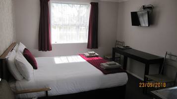 A hotel room with a bed, a desk, a chair, a TV, and a window with curtains.