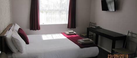 A hotel room with a bed, a desk, a chair, a TV, and a window with curtains.