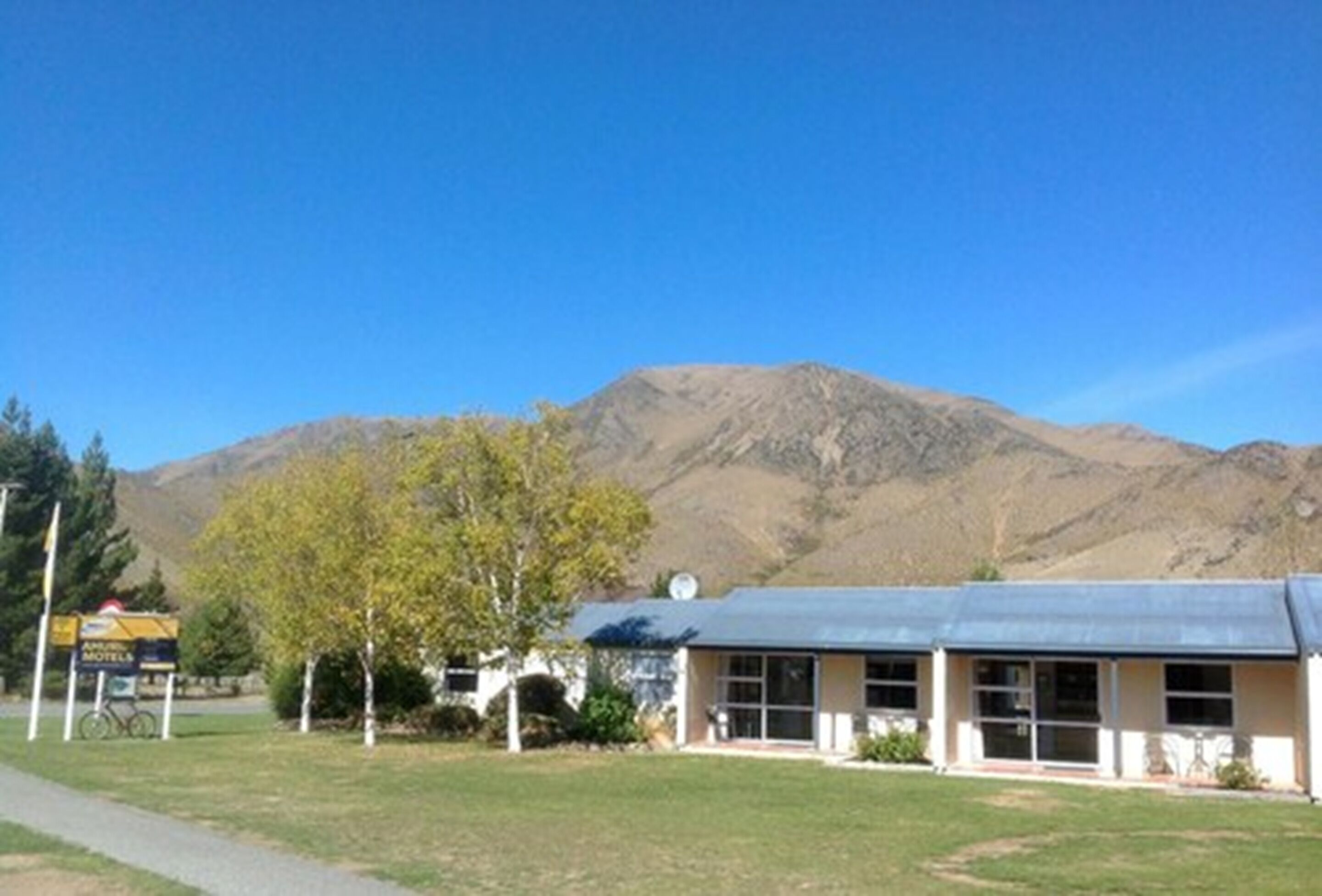 A motel with a simple, single-story structure, a paved driveway, and a mountain backdrop.
