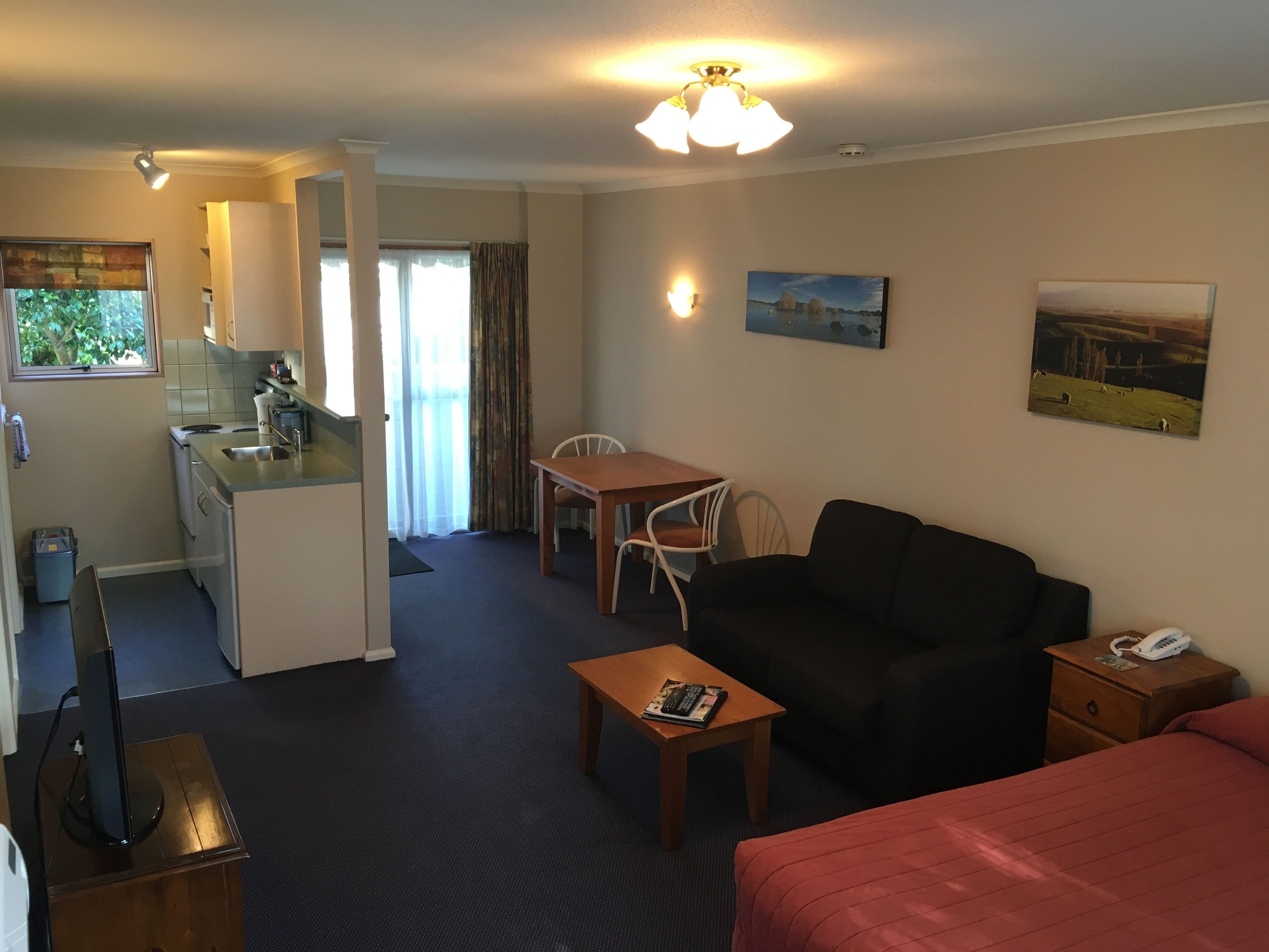 Et kompakt hotelværelse med tekøkken, spiseplads, sofa, lille bord og seng.