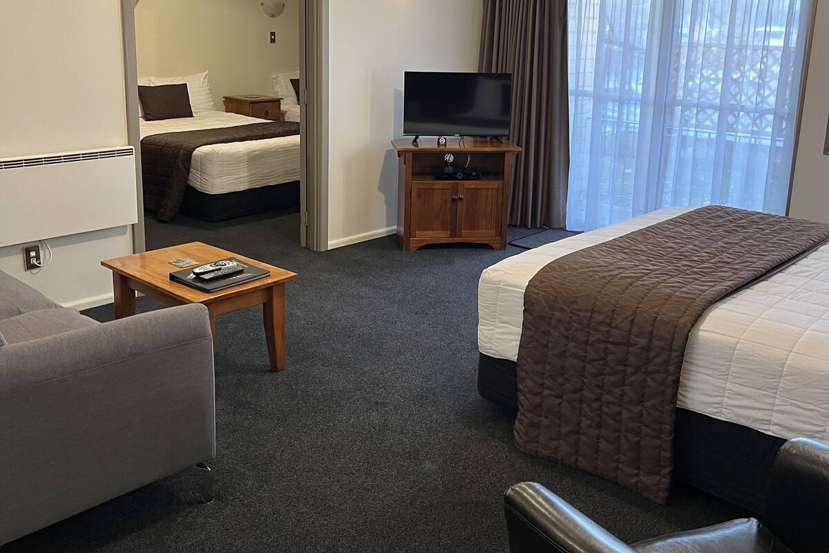 A hotel room with a bed, a sofa, a TV, a small table, and a window with curtains.