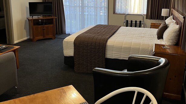Ein Hotelzimmer mit einem Bett, einem Fernseher auf einem Schrank, einem Schreibtisch mit Stuhl und einem Vorhangfenster.