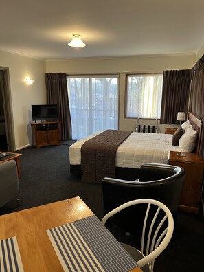 A hotel room with a bed, a TV on a stand, a desk with a chair, and a window with curtains. - Parklands Motor Lodge Timaru (Timaru)