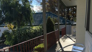 Ein Balkon mit Glastisch und Metallstühlen, der auf einen Parkplatz und Bäume blickt.