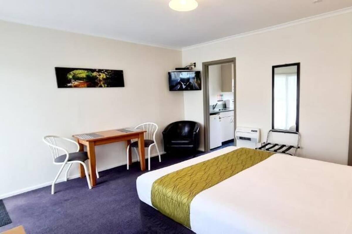 A hotel room with a bed, a desk with chairs, a television, a wardrobe, and a mirror.