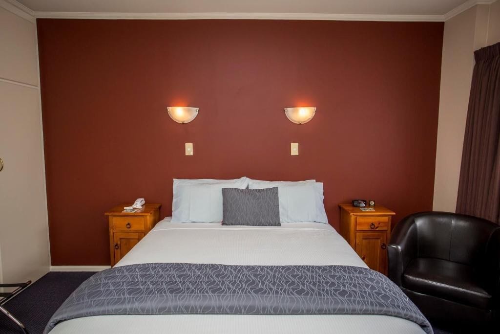 A hotel room with a large bed, two bedside tables, a chair, and wall-mounted lights.