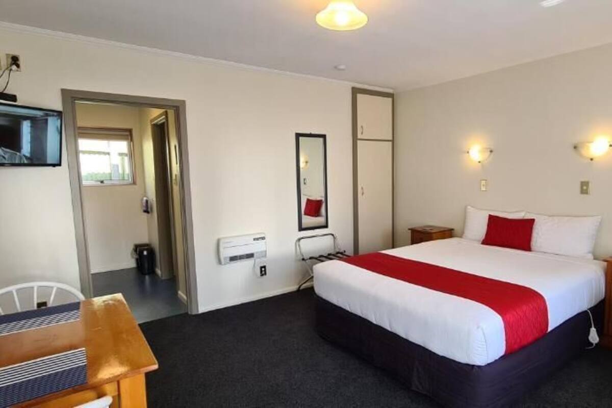 A hotel room with a bed, a desk, a chair, a TV, and a mirror.