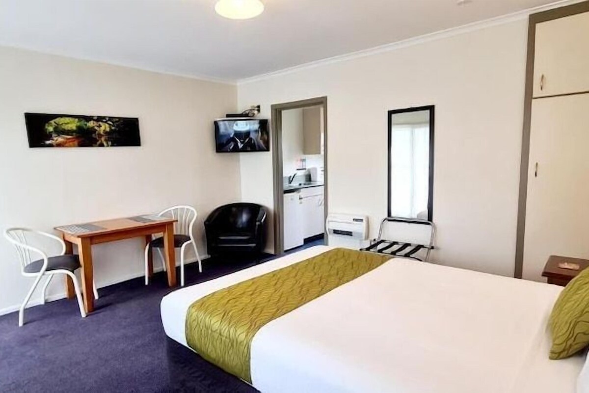 A hotel room with a bed, a desk, a chair, a television, and a wardrobe.