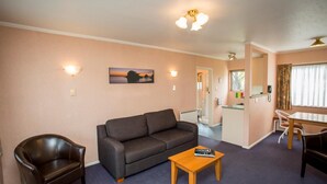Ein Wohnzimmer mit einer Couch, einem Couchtisch und einem Sessel. An der Wand hängt ein Gemälde und ein Fenster mit Vorhängen.