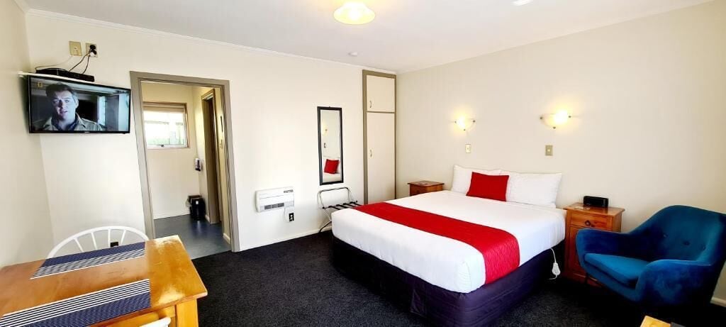Ein Hotelzimmer mit Bett, Schreibtisch, Stuhl, Fernseher und Spiegel.