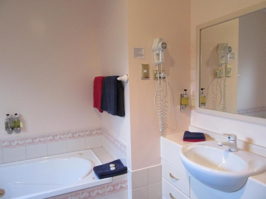 A bathroom with a bathtub, a sink, and a hairdryer mounted on the wall.