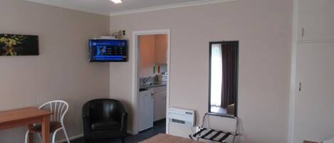 Habitación de hotel con cama, escritorio, silla, televisor, espejo y una pequeña kitchenette.