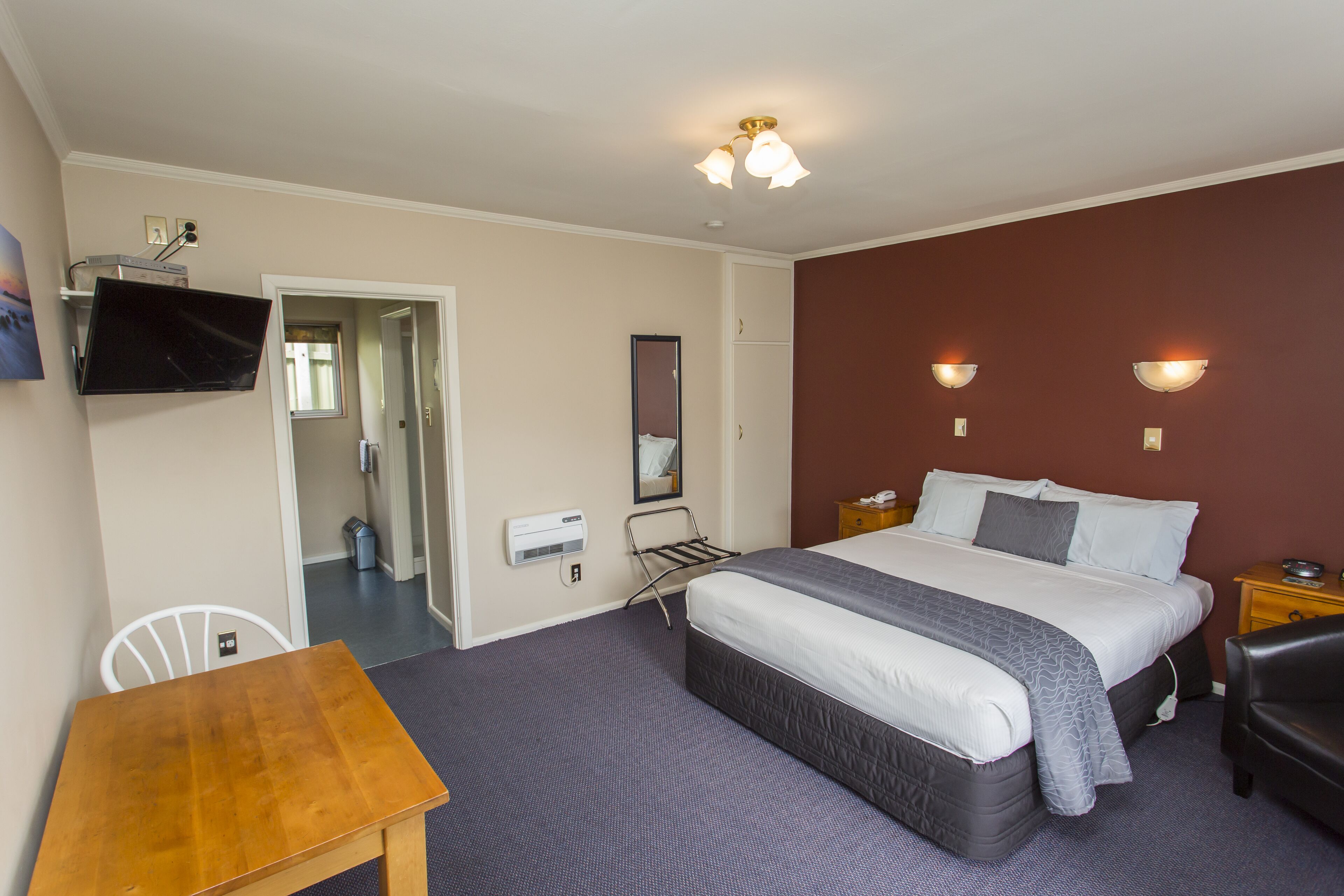 Hotelkamer met een bed, bureau, stoel, tv aan de muur en een spiegel.