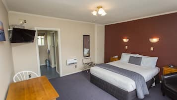 Hotelkamer met een bed, bureau, stoel, tv aan de muur en een spiegel.