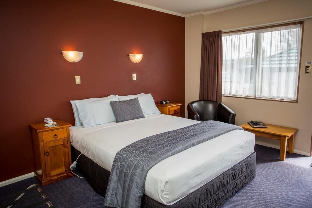 Quarto de hotel com uma cama grande, duas luminárias de cabeceira, uma escrivaninha e uma cadeira.