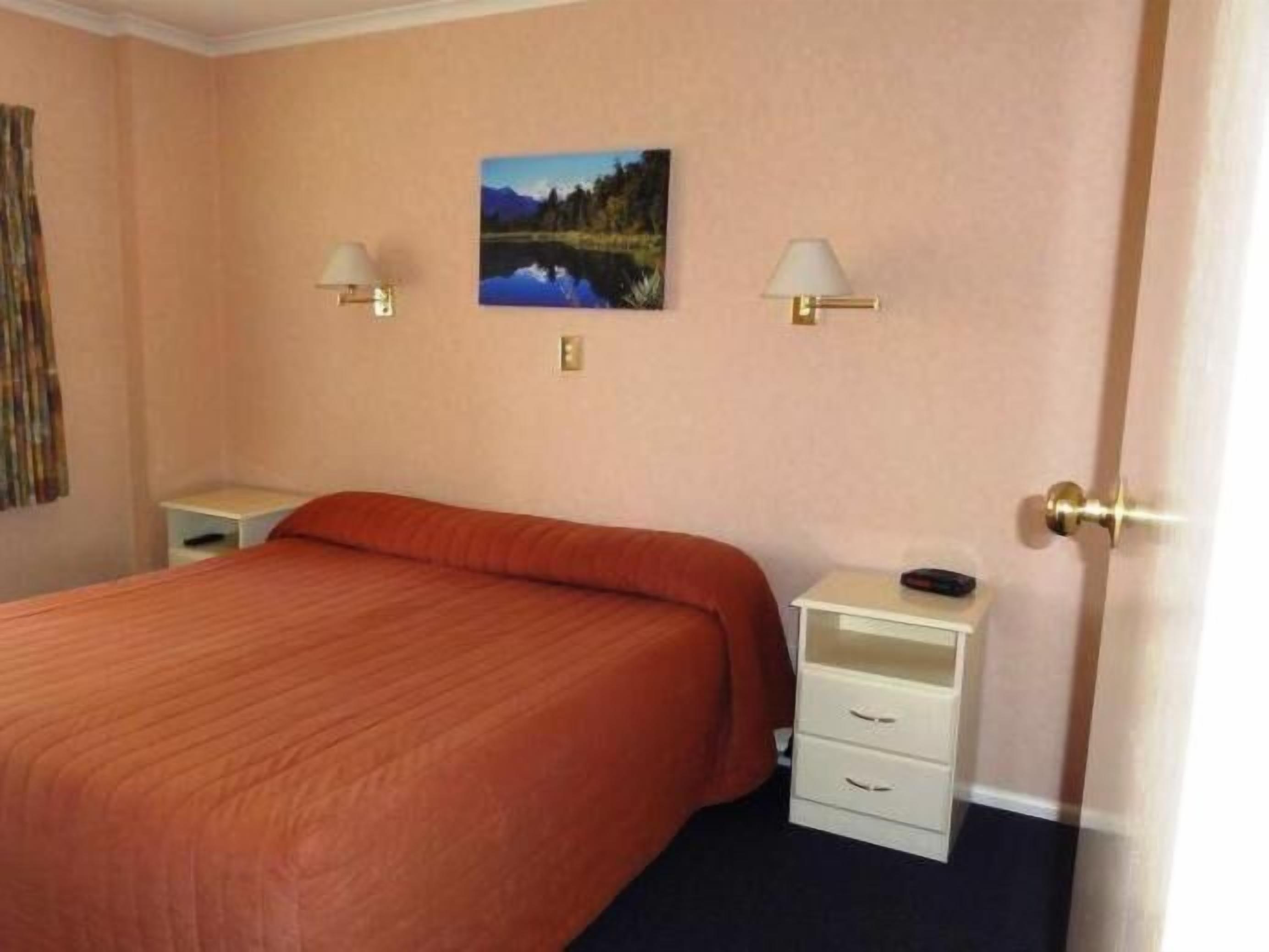 Een slaapkamer met een bed, twee nachtkastjes, een wandlamp en een schilderij.