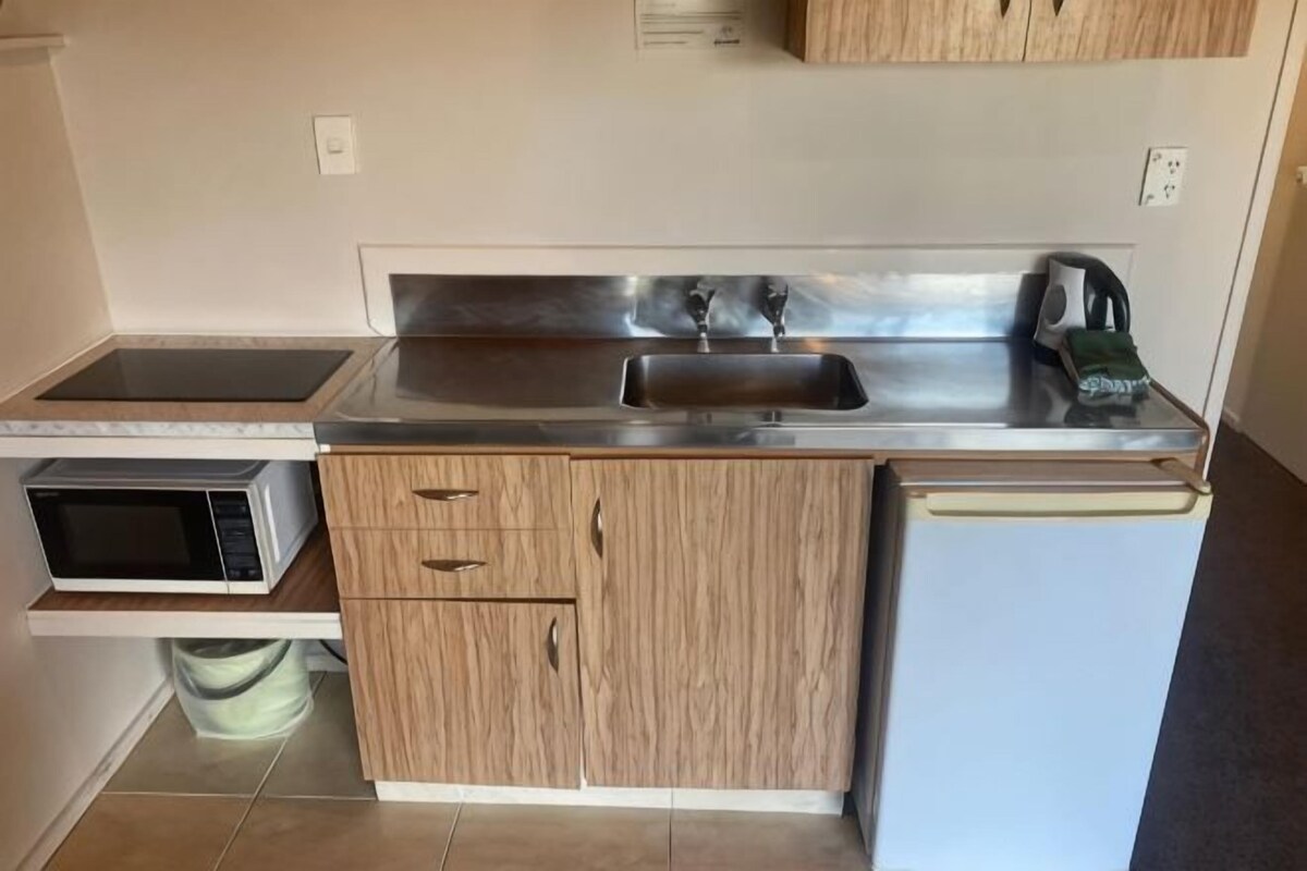 A compact kitchen with a microwave, sink, and a kettle.