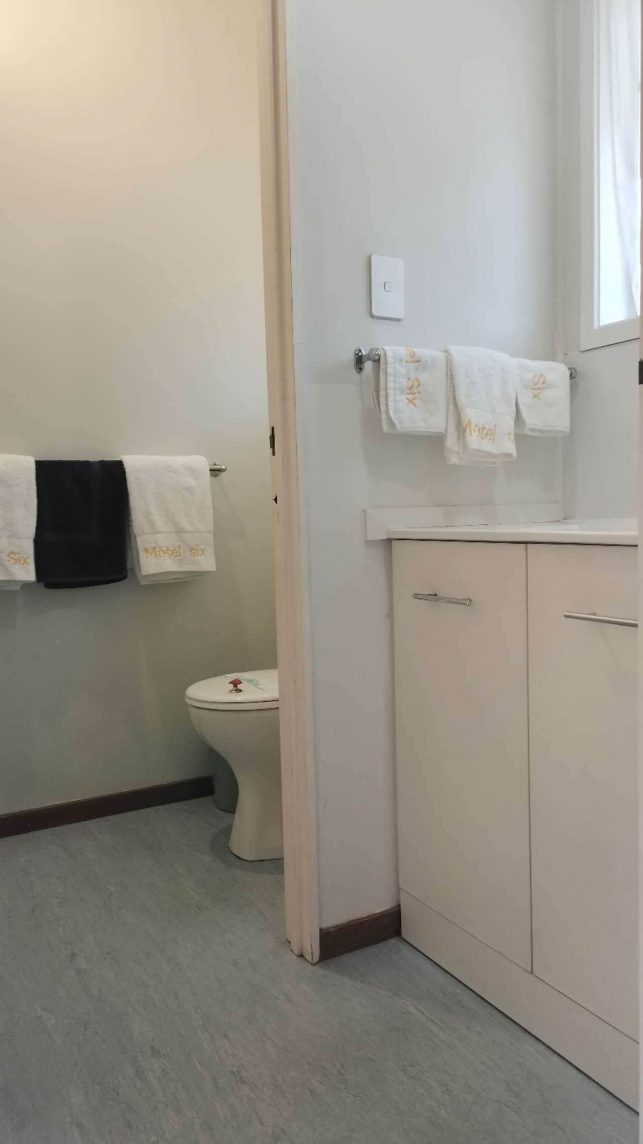 A bathroom with a toilet, a sink, and a mirror. There are towels hanging on the wall and a door leading to another room.