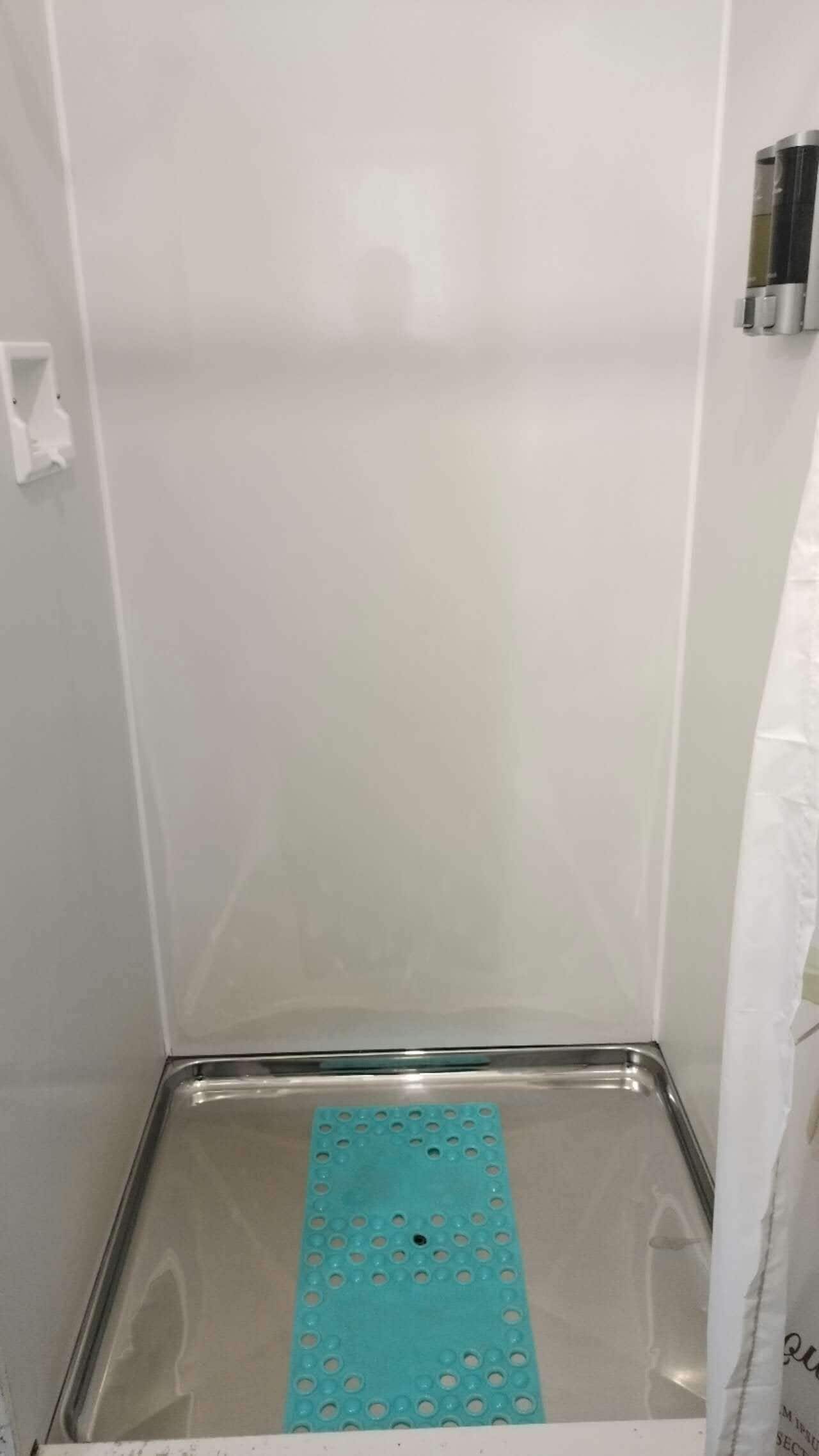 A bathroom with a white tiled wall, a stainless steel shower tray, and a blue shower mat.