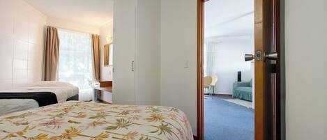 A hotel room with a bed, a desk, a chair, and a view of another room through an open door.