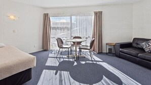 Une chambre d’hôtel avec un lit, une table ronde entourée de chaises, un canapé en cuir noir et une petite table d’appoint.