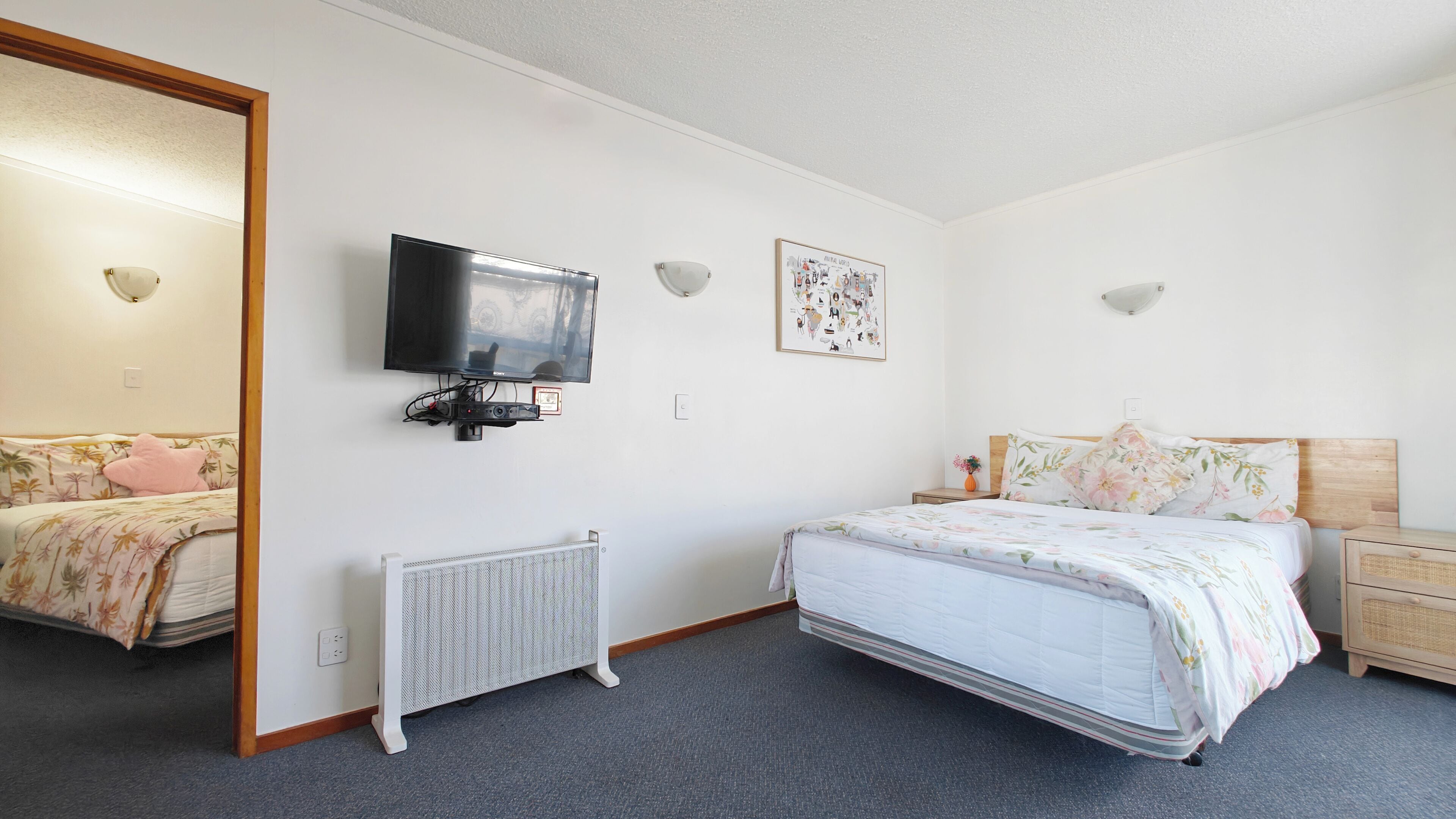 A bedroom with a bed, a television mounted on the wall, a radiator, and a framed picture.