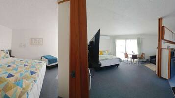 Quarto de hotel com duas camas, uma escrivaninha, uma cadeira e uma cozinha compacta.